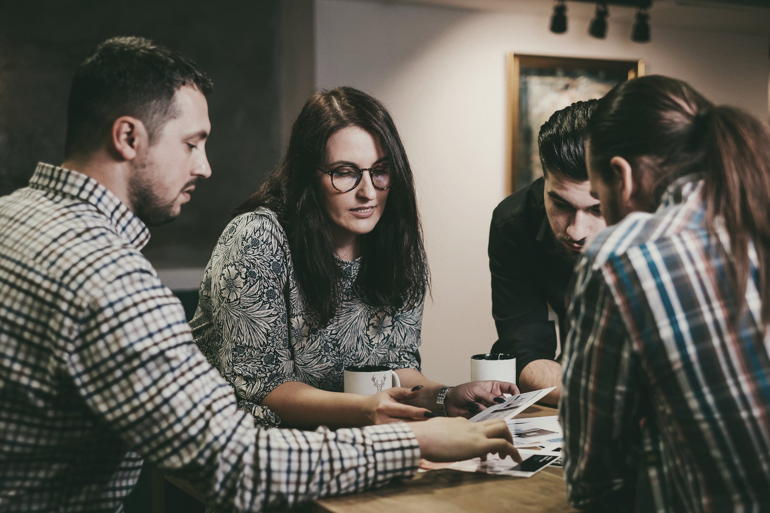 Four colleagues reviewing papers together at a table, mid-discussion