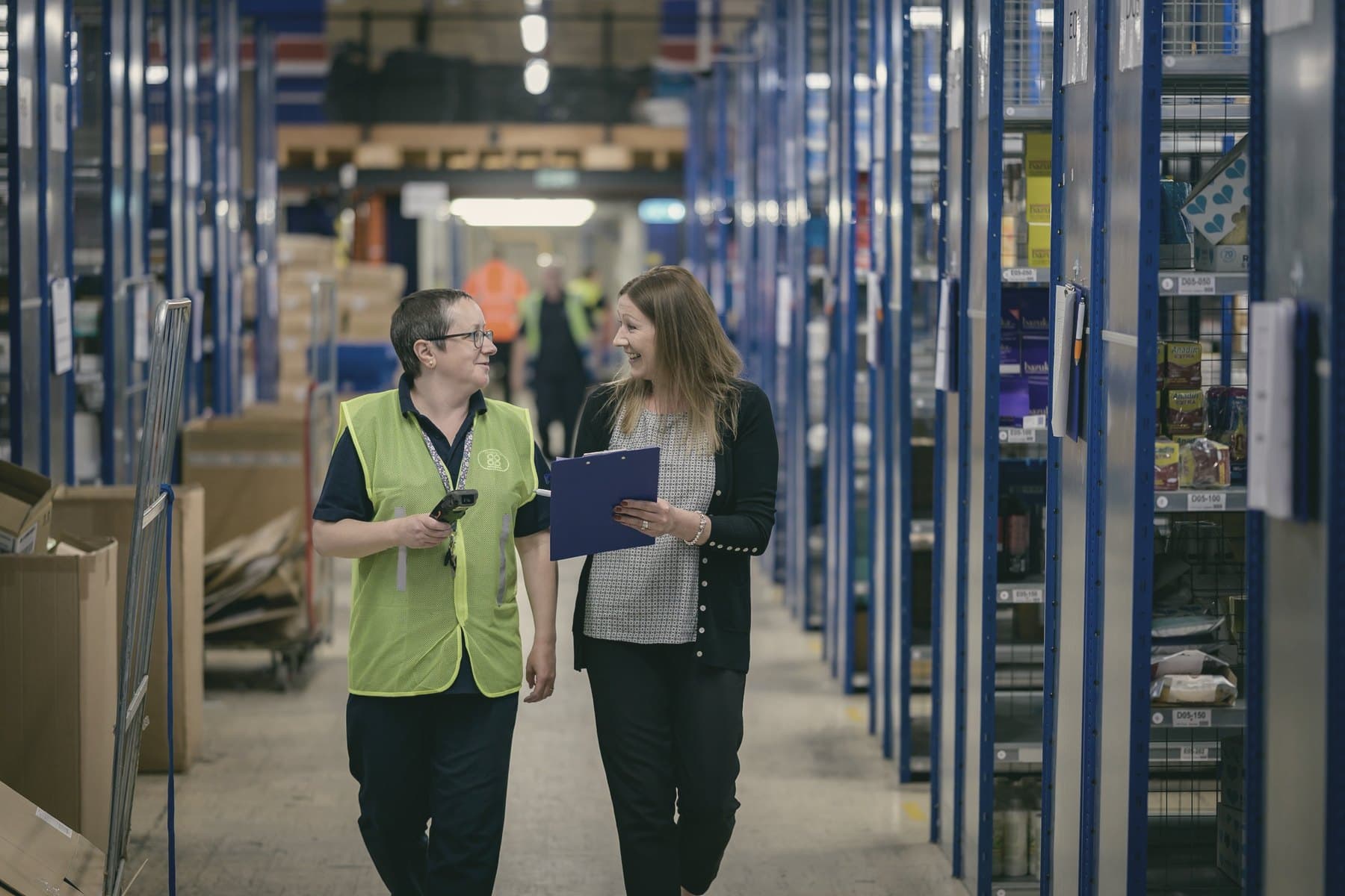 A manager and a team member walking through a warehouse, one holding a clipboard