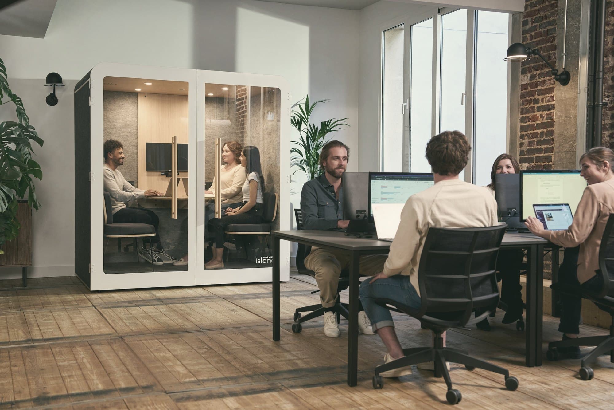 A working office, people at their desks and a meeting booth