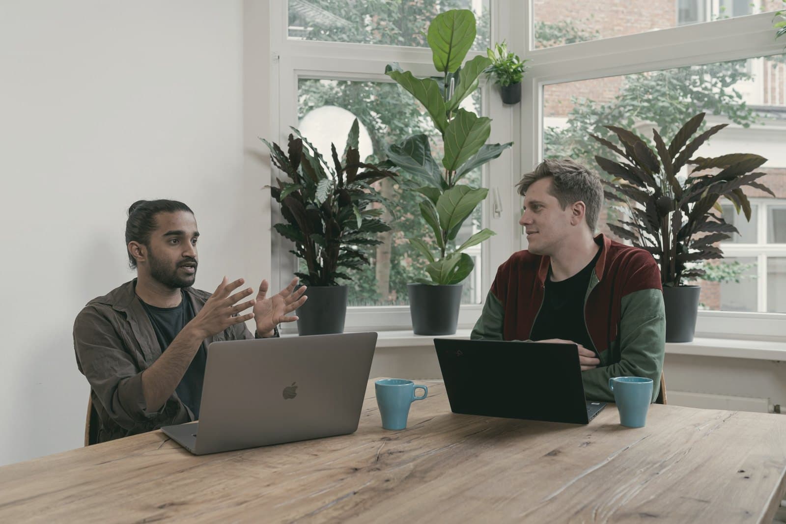 Two colleagues talking something through across a table, laptops open